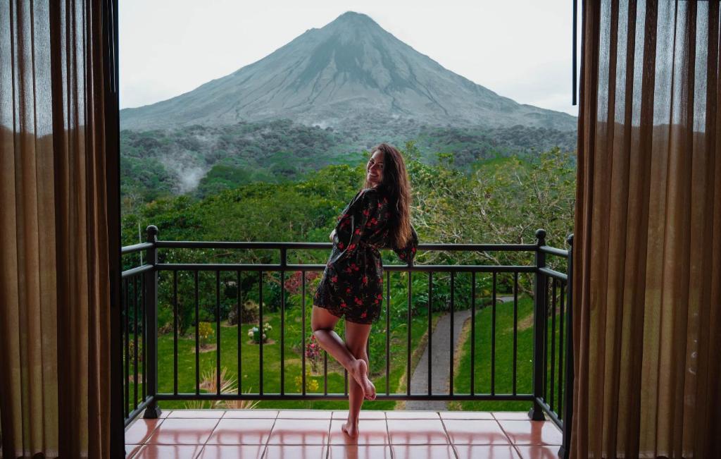 Una mujer parada en un balcón con vistas a una montaña en Hotel Arenal Kioro Suites & Spa en Fortuna