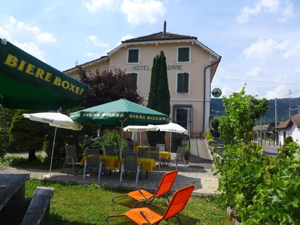 eine Gruppe von Stühlen und Sonnenschirmen vor einem Gebäude in der Unterkunft Hôtel-Restaurant de la Gare in Glovelier