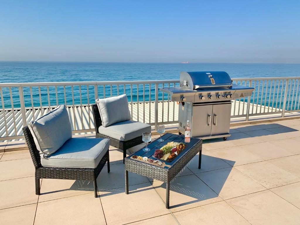 a grill and two chairs on a deck with the beach at Escape to our Happy Place on Umdloti Beach in Umdloti