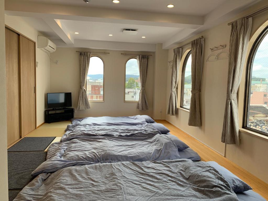 two beds in a bedroom with windows and a tv at オレンジの風 in Imabari
