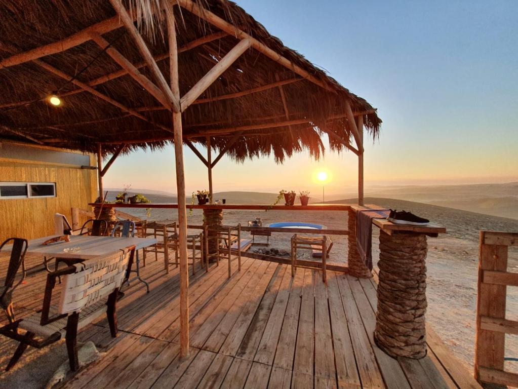 een houten terras met tafels en een rieten paraplu bij רוח מדבר - Desert wind in Dimona
