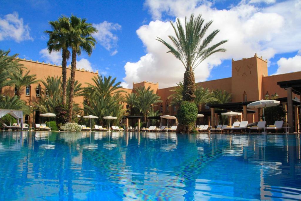 ein großer Pool mit Palmen und Sonnenschirmen in der Unterkunft Berbère Palace in Ouarzazate