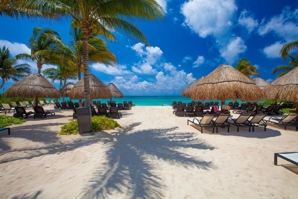 una playa con sillas y sombrillas y el océano en The Elements Oceanfront & Beachside Condo Hotel, en Playa del Carmen