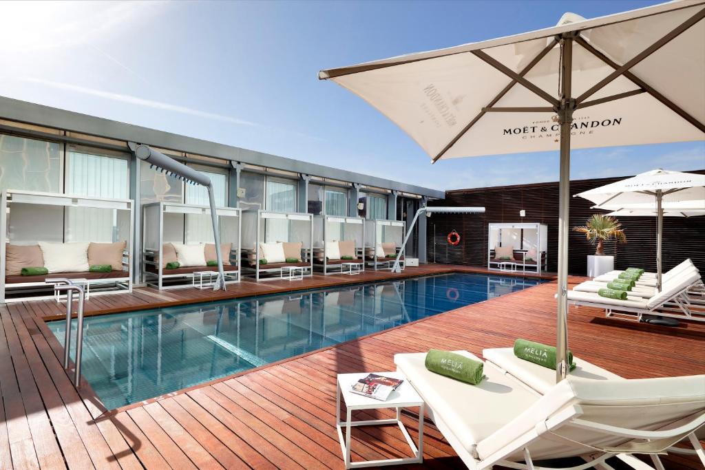 a pool with chairs and an umbrella in a building at Melia Barcelona Sky 4* Sup in Barcelona