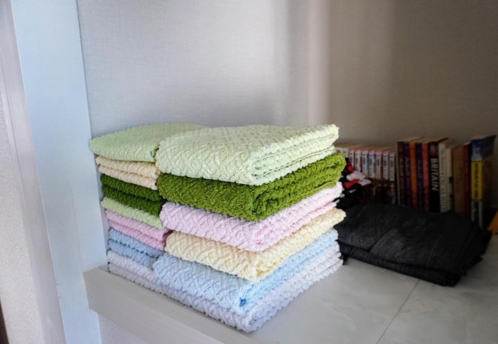 a stack of towels sitting on a shelf next to a bookcase at ゲストハウス庵（いおり）大阪 