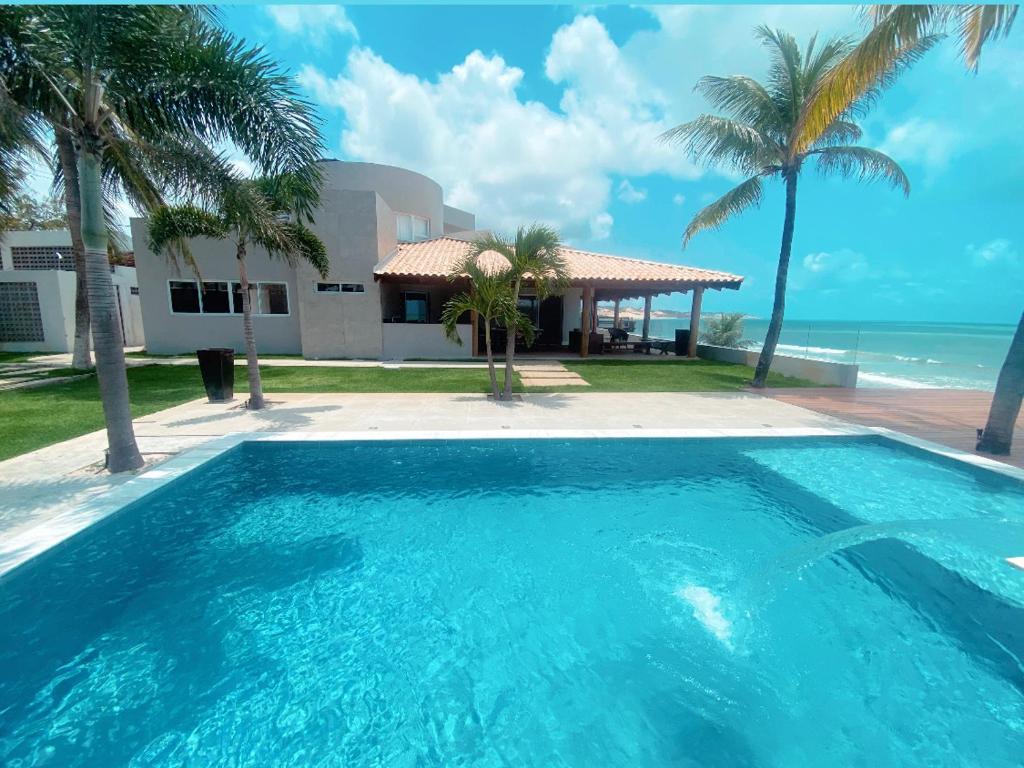 a swimming pool in front of a house and the ocean at Luxo e pé na areia in Parnamirim