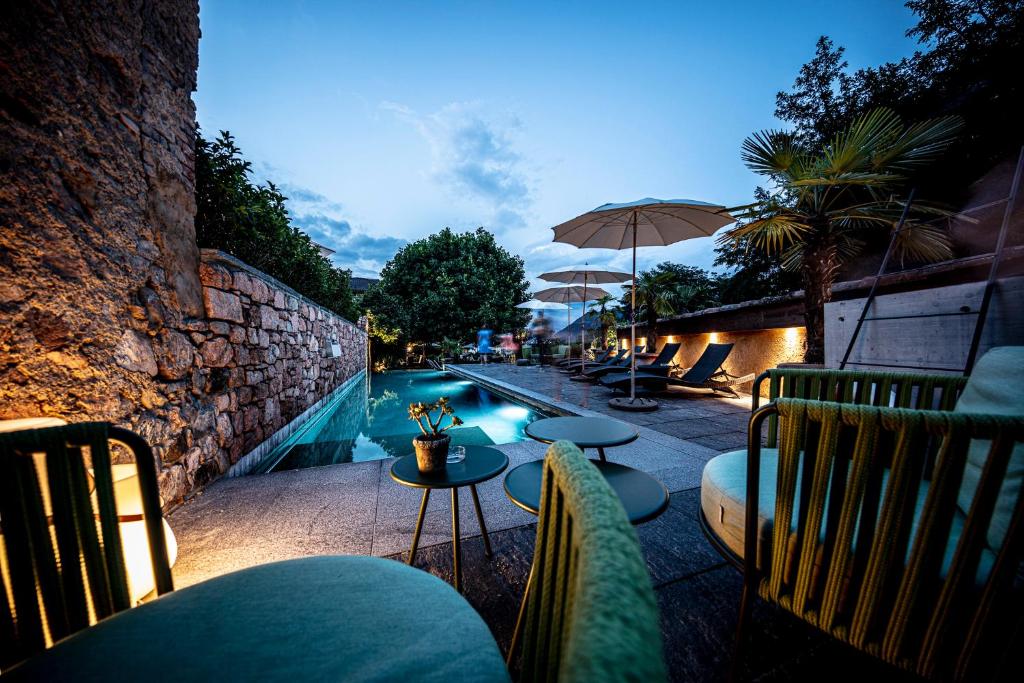 einen Pool mit Stühlen, einem Tisch und einem Sonnenschirm in der Unterkunft Swiss Historic & Garten Hotel Villa Carona in Carona