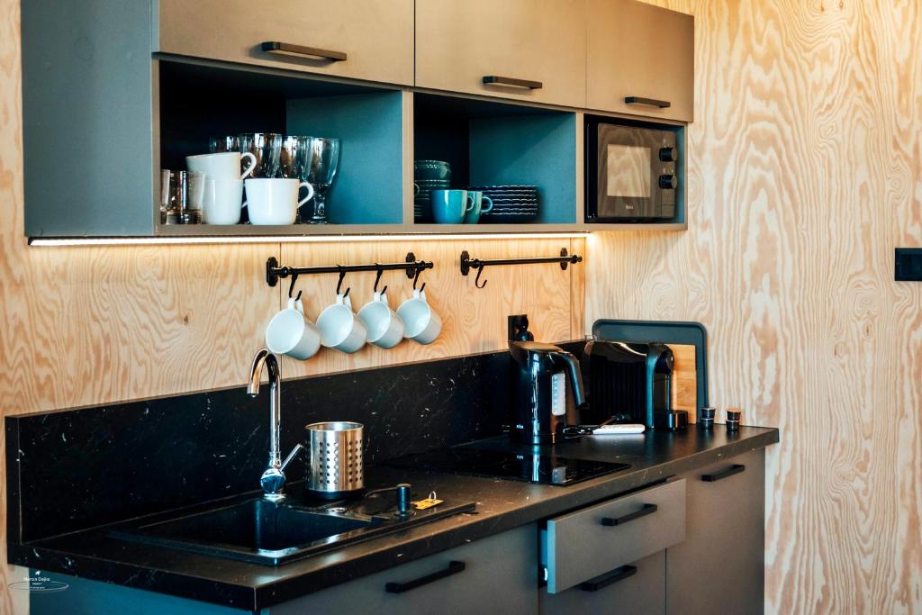 Compact modern kitchenette with black countertop, hanging mugs, glassware and coffee machine.