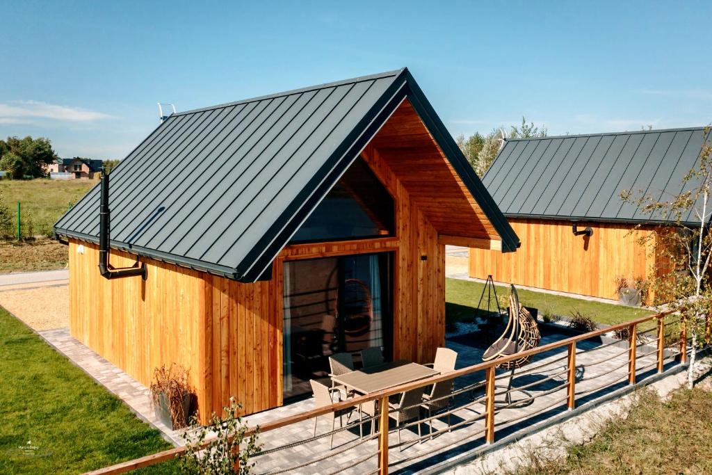 Wooden A-frame cabin with dark metal roof, patio dining set and hanging chair on deck.