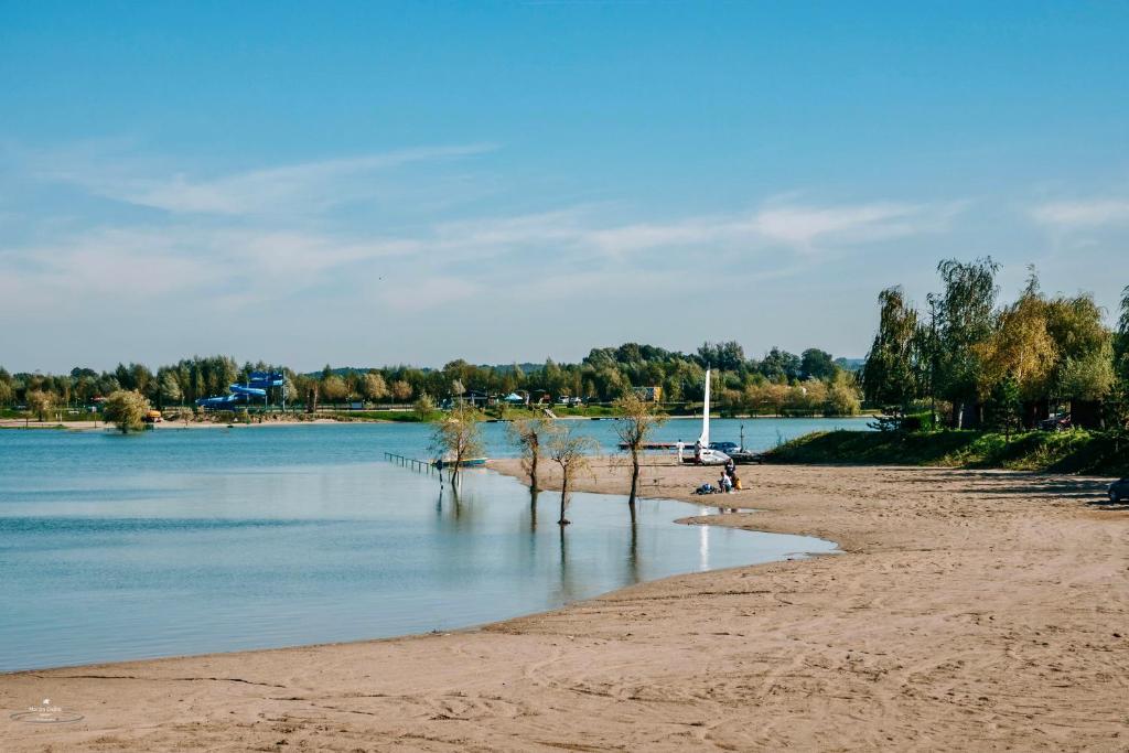 Calm sandy lakeshore with sailboat, small group on beach, trees and distant treeline.