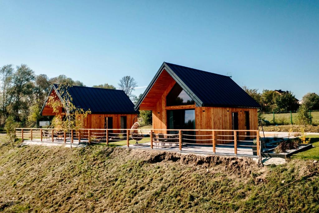 Two wooden A-frame cabins on raised deck with railing, patio furniture, and grassy hill.