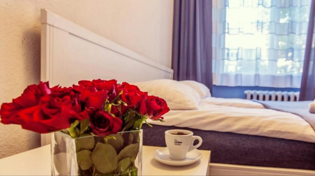 a vase of red roses on a table next to a bed at Apartamenty Spodek in Katowice