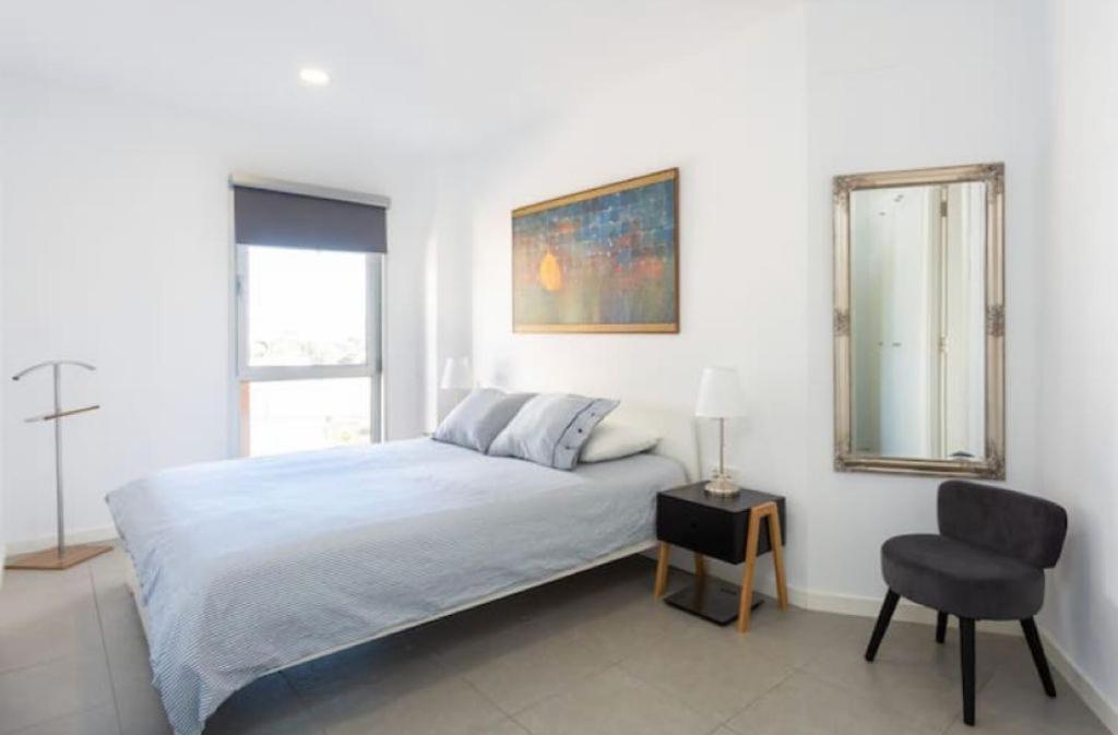 a white bedroom with a bed and a chair at Modern seafront flat with a private garage in El Médano