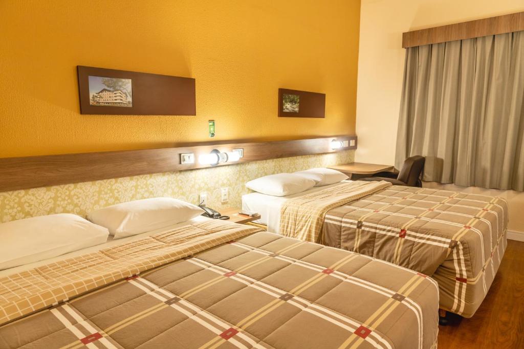 two beds in a hotel room with yellow walls at Hotel 10 Blumenau in Blumenau