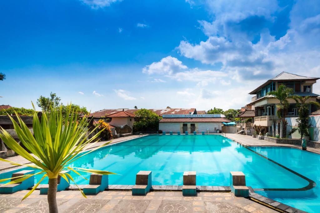 a large swimming pool with a palm tree in front of a house at Mahajaya Hotel Denpasar in Denpasar