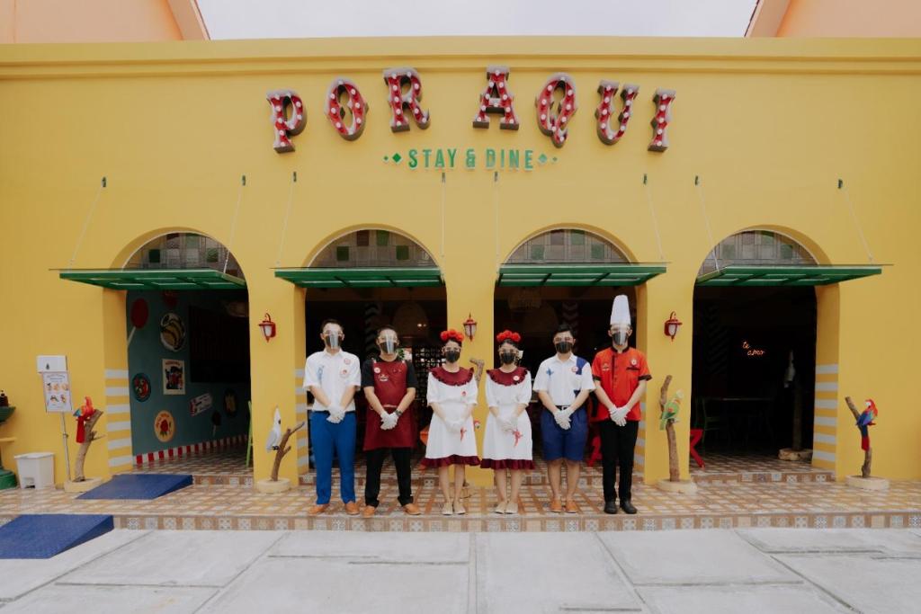 Por Aqui Stay & Dine في Timuran: مجموعة اشخاص واقفين امام مبنى اصفر