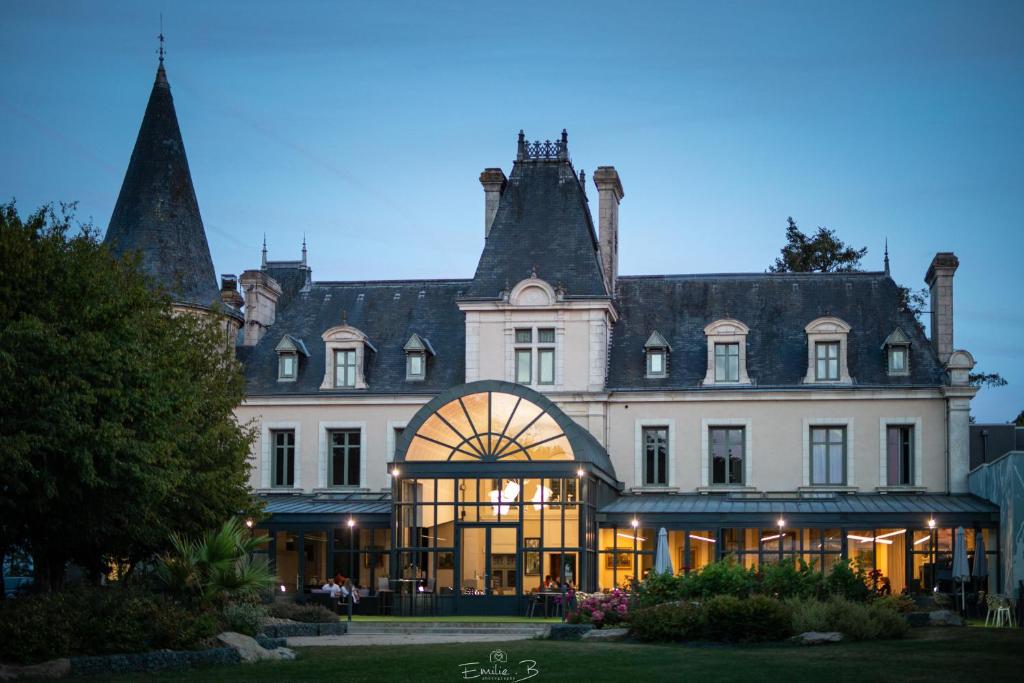 un grand bâtiment blanc avec une tour d'horloge dans l'établissement Hotel Château de la Barbinière, à Saint-Laurent-sur-Sèvre