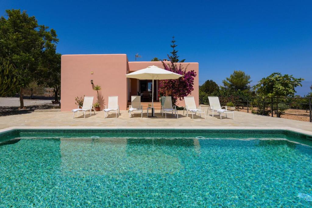 a swimming pool with chairs and an umbrella and a house at Miquela in Es Cana