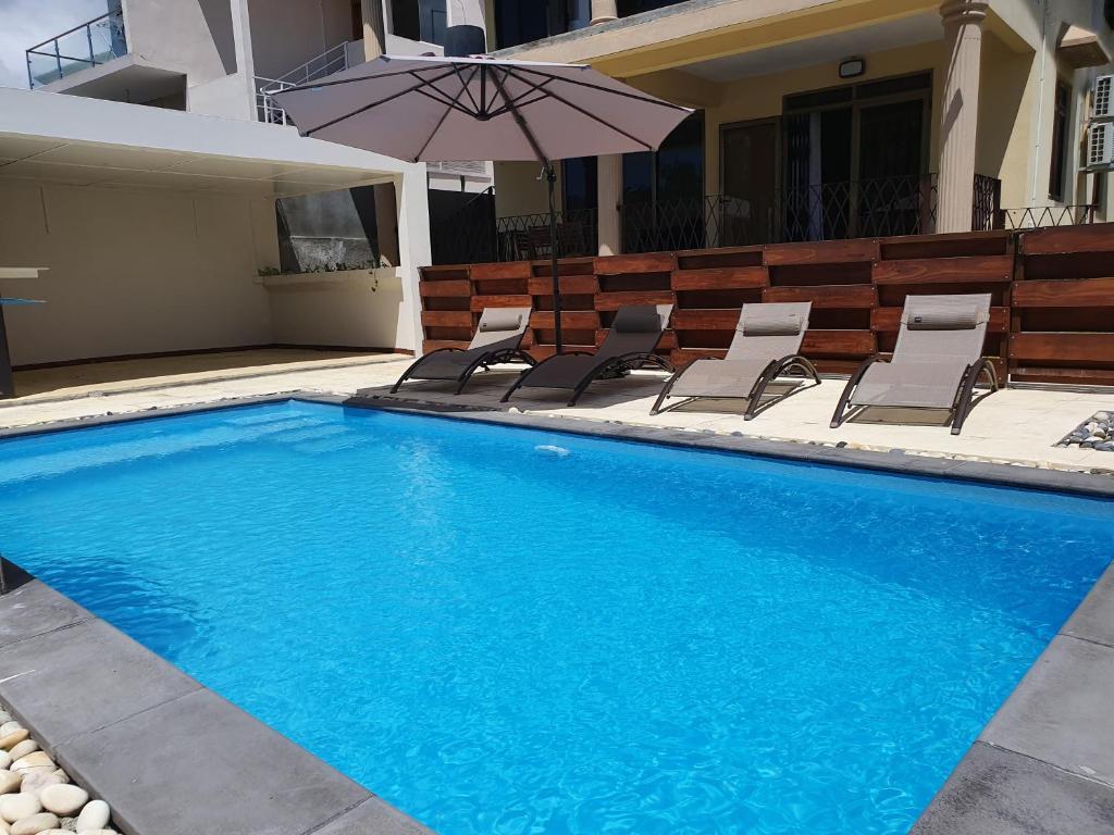 a swimming pool with chairs and an umbrella next to a house at Villa Oceane in Pereybere