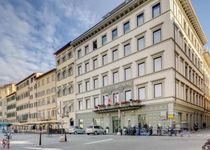 un grand bâtiment blanc au coin d'une rue dans l'établissement Hotel Roma, à Florence