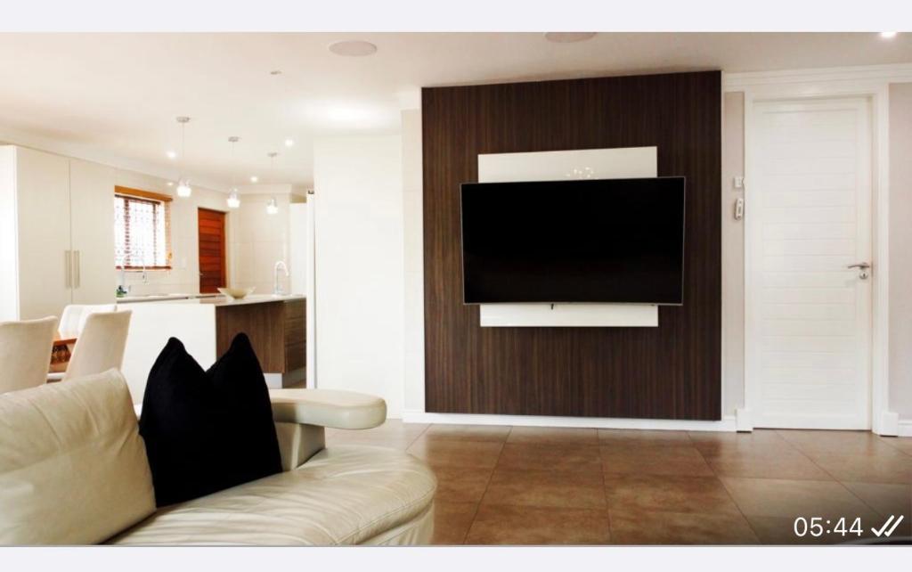 een woonkamer met een bank en een televisie aan de muur bij Precious Paradise Villa in Amanzimtoti