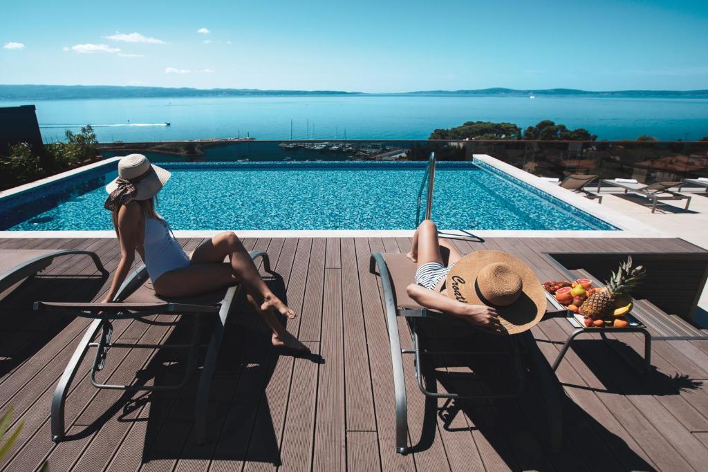 two women sitting in chairs next to a swimming pool at Marvie Hotel & Health in Split