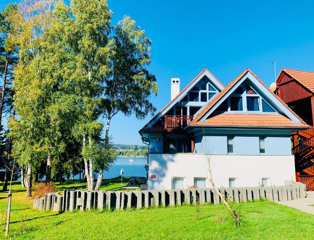 a house with a fence in front of a lake at RIVIERA LIPNO 502 Apartmán 4kk u vody in Lipno nad Vltavou