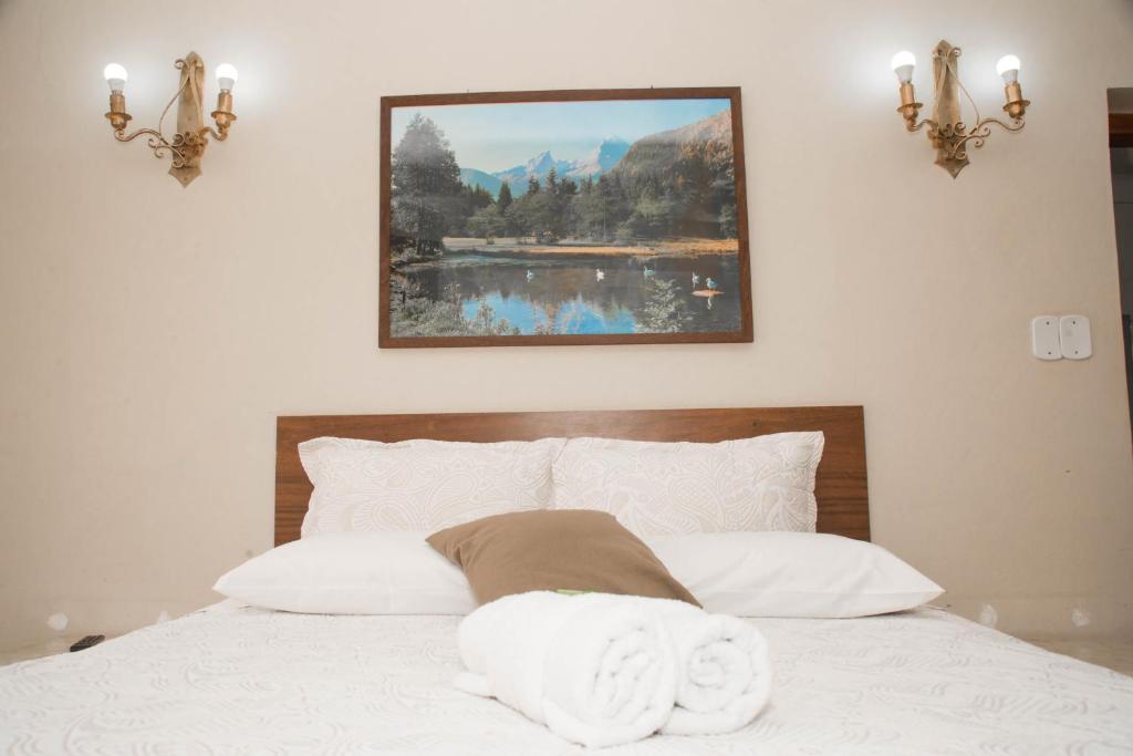 a bed with white pillows and a picture on the wall at Pousada FM - Vila Capivari in Campos do Jordão