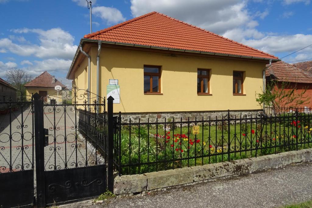 a yellow house with a black fence and flowers at Borostyán Vendégház in Alsóregmec