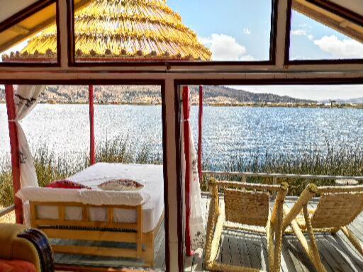 Blick auf das Wasser aus einem Fenster mit einem Bett und Stühlen in der Unterkunft Uros Qhota Uta Lodge in Puno