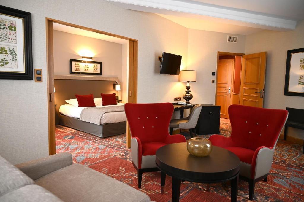 トゥールニュにあるHôtel Le Rempartのベッドと赤い椅子が備わるホテルルームです。