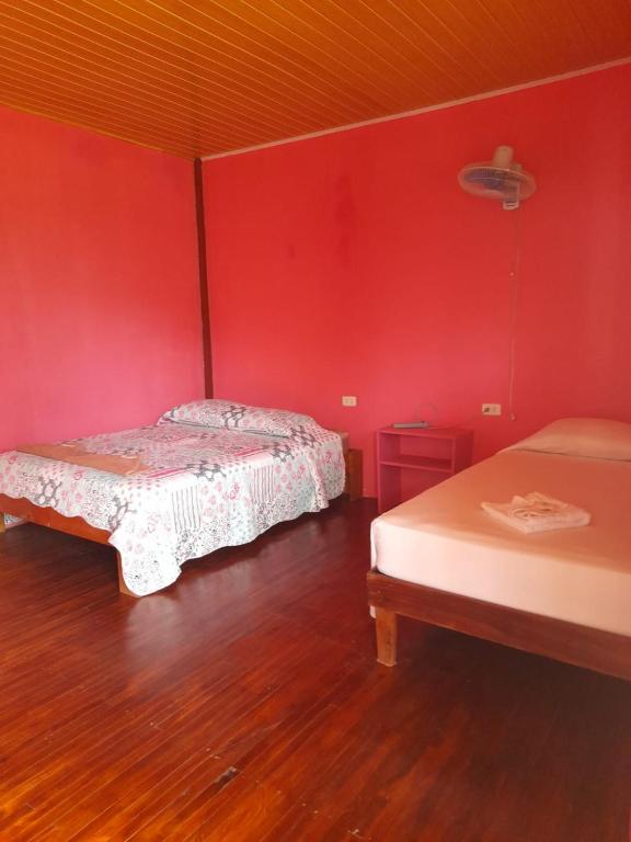 two beds in a room with red walls and wooden floors at Hostal & Cabins Lidia's House, Forest and Ocean View in Drake