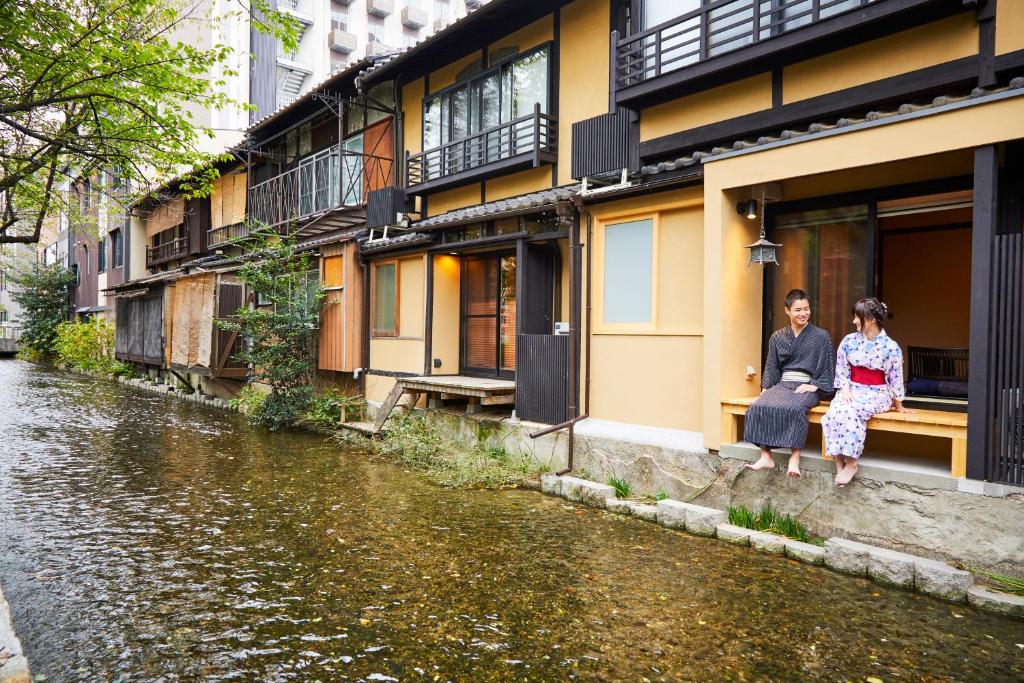 a man and woman sitting on a ledge next to a river at Rinn Shijo Takase River North in Kyoto