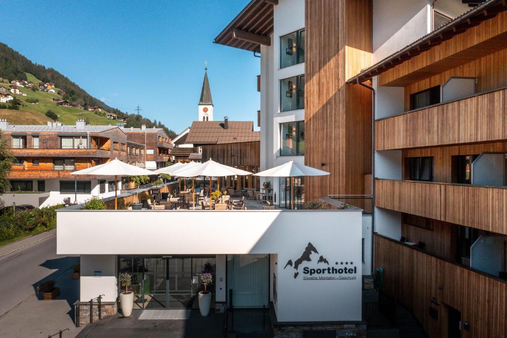 une vue extérieure d'un bâtiment avec des tables et des parasols dans l'établissement Sporthotel Silvretta Montafon, à Gaschurn