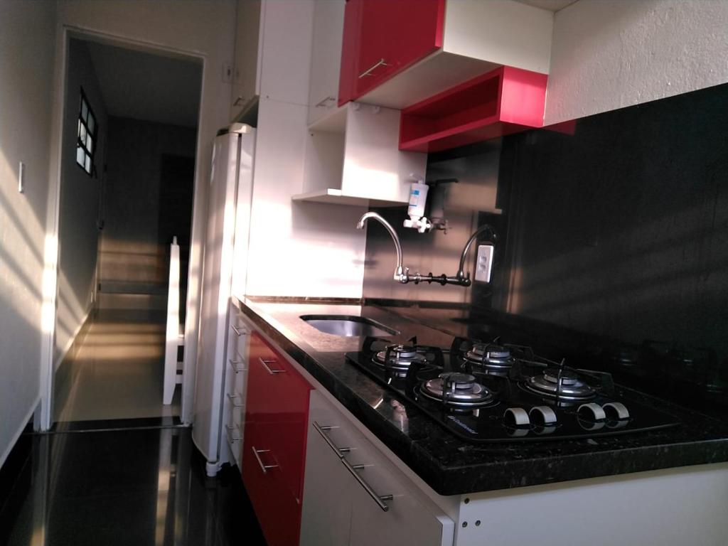 Il comprend une cuisine équipée d'une cuisinière, d'un évier et de placards rouges. dans l'établissement LA15-Bertioga, Próximo ao SESC, Riviera, Vista Linda, Indaiá, à Bertioga