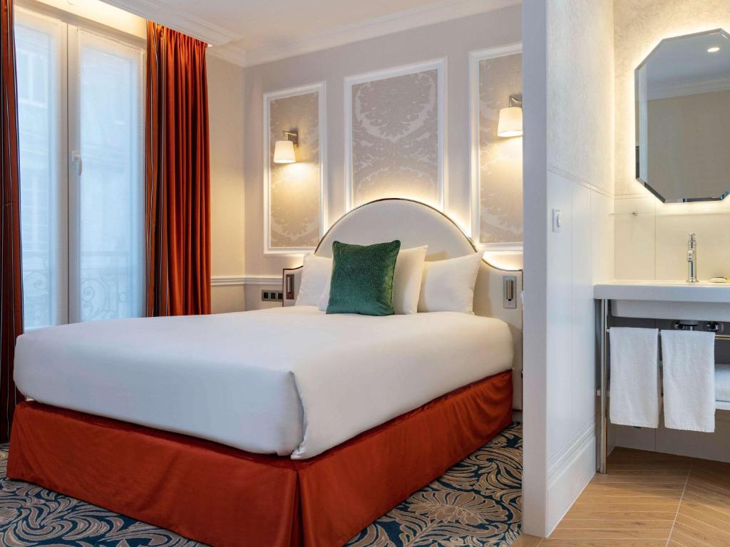 パリにあるホテル メルキュール ラ ソルボンヌ サンジェルマン デ プレの大型ベッドとシンクが備わるホテルルームです。