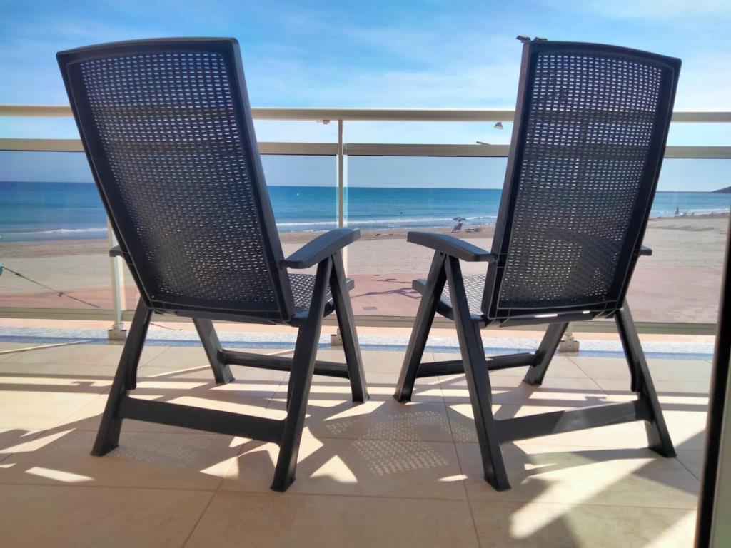 two chairs sitting on a balcony overlooking the beach at PINEDA BEACH 1a línea de mar & parking in La Pineda