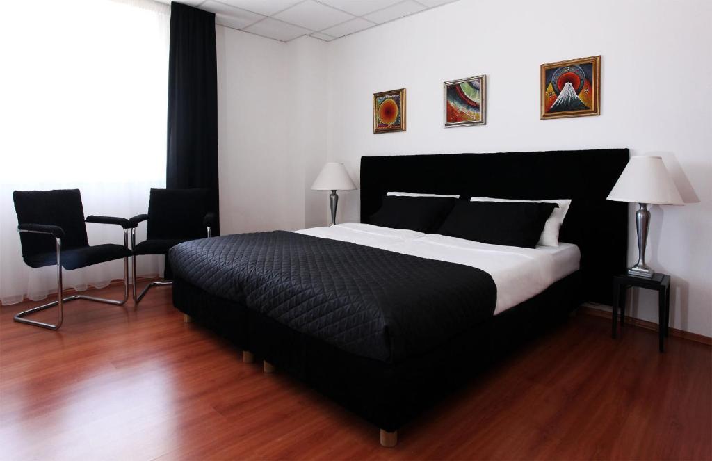 a bedroom with a large black bed and two chairs at Sós Motel in Hatvan