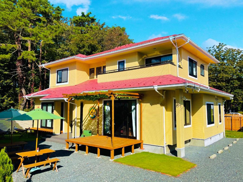 una casa amarilla con dos mesas de picnic delante de ella en Guesthouse Murabito en Yamanakako