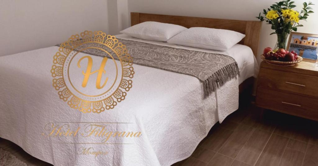 a bed with a white blanket and a gold insignia on it at Hotel Filigrana Mompox in Mompos