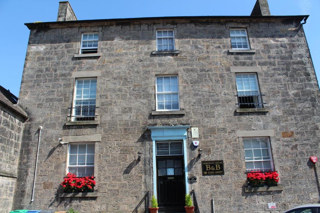 un antiguo edificio de piedra con flores rojas en las ventanas en Merchant House, en Kirkcaldy