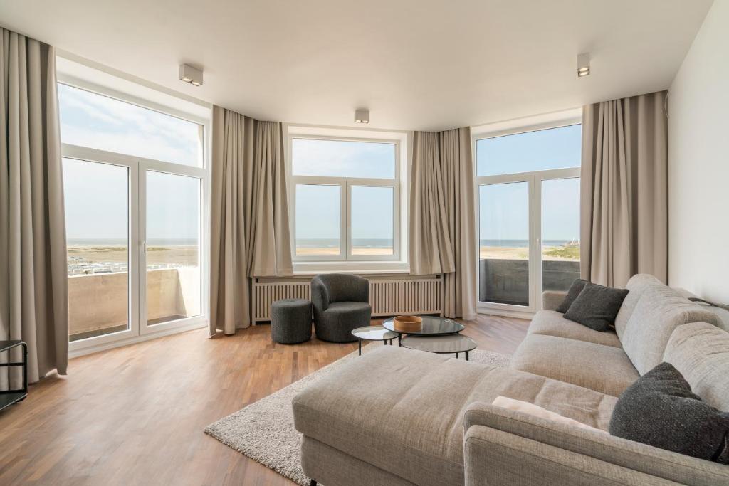 een woonkamer met een bank en een aantal ramen bij Residence Palace Style app in a unique building in Zeebrugge