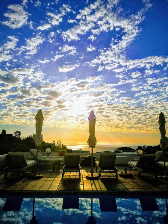 a pool with chairs and umbrellas and the sunset at Diamond House Guesthouse in Cape Town
