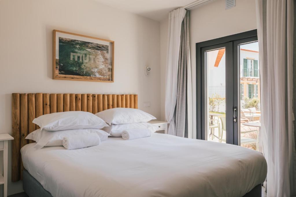a bedroom with a large bed with white sheets and pillows at MUTE Hostel Porto Covo in Porto Covo
