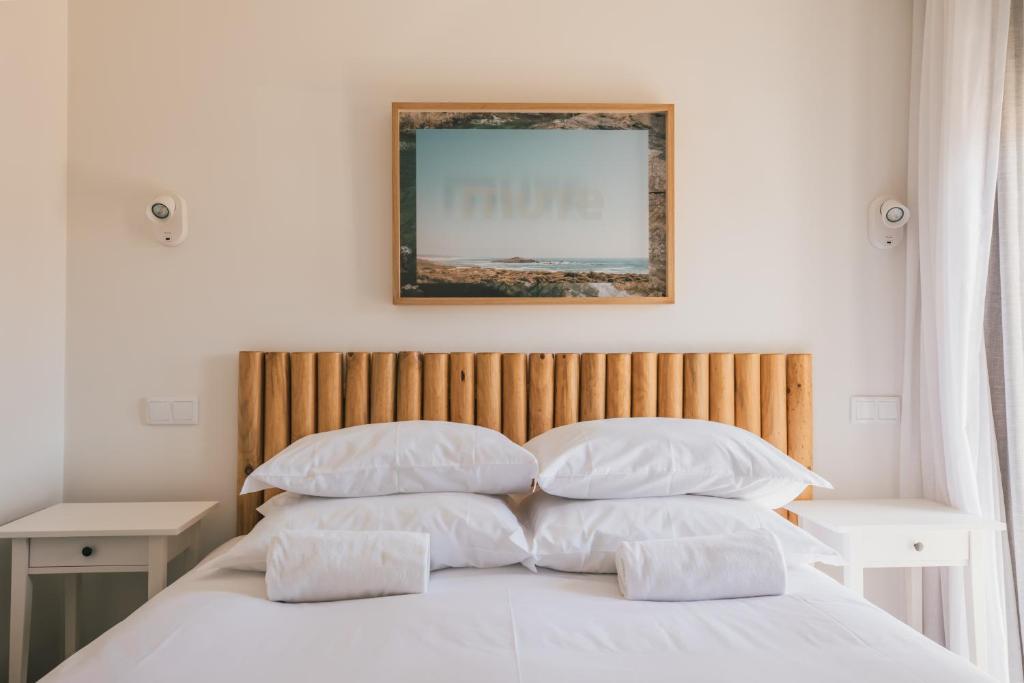 a bed with white pillows and a picture on the wall at MUTE Hostel Porto Covo in Porto Covo