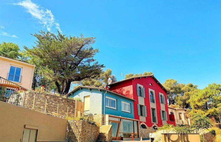 a red and blue building with trees in the background at Hotel Le Bon Port in Collioure