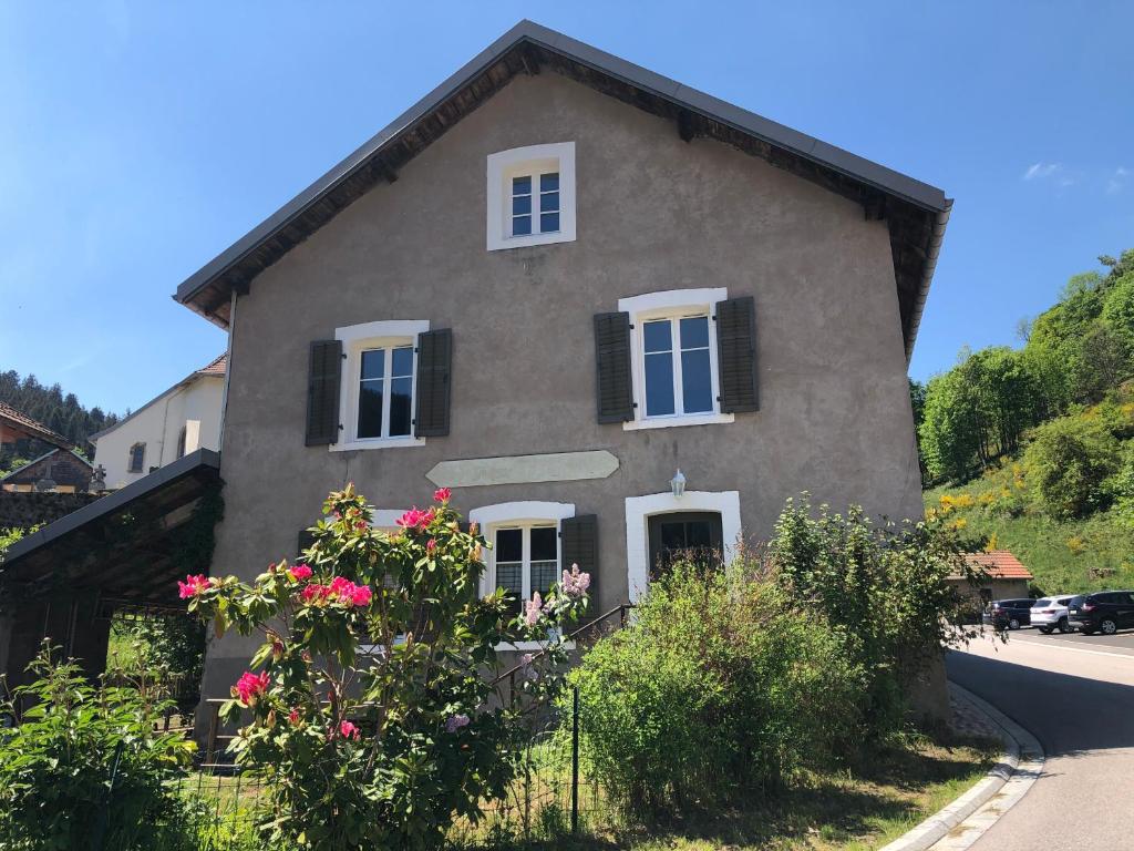 ein Steinhaus mit schwarzen Fensterläden und rosa Blumen in der Unterkunft Le Valtinet, séjour esprit montagne in Le Valtin