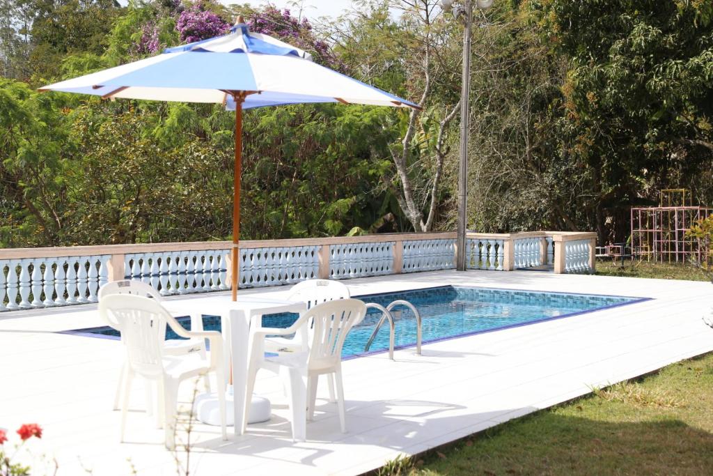 a table and chairs with an umbrella next to a pool at Sítio Belucci in Pinhalzinho