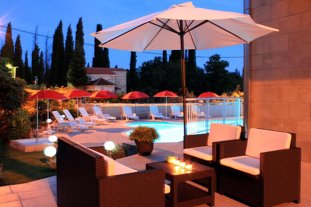 a patio with chairs and an umbrella and a pool at Apartments Grand Pinea in Čilipi