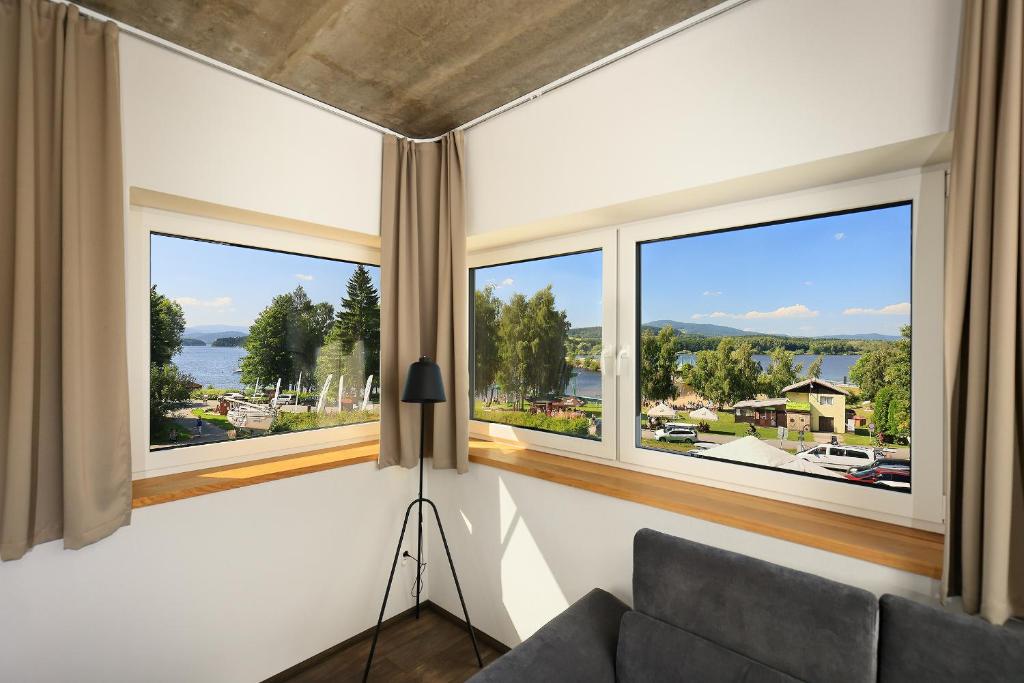a living room with large windows and a couch at Apartmány Panelka Costa Plana Lipno in Černá v Pošumaví
